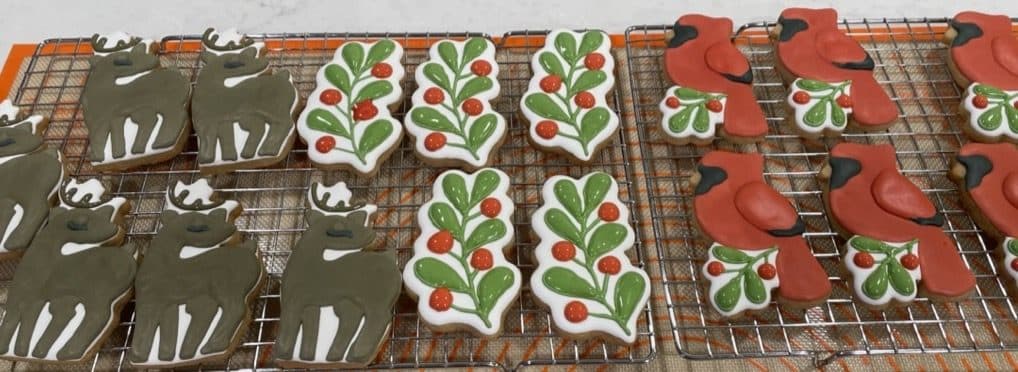 Christmas tree, cat, and holly cookies cooling on racks